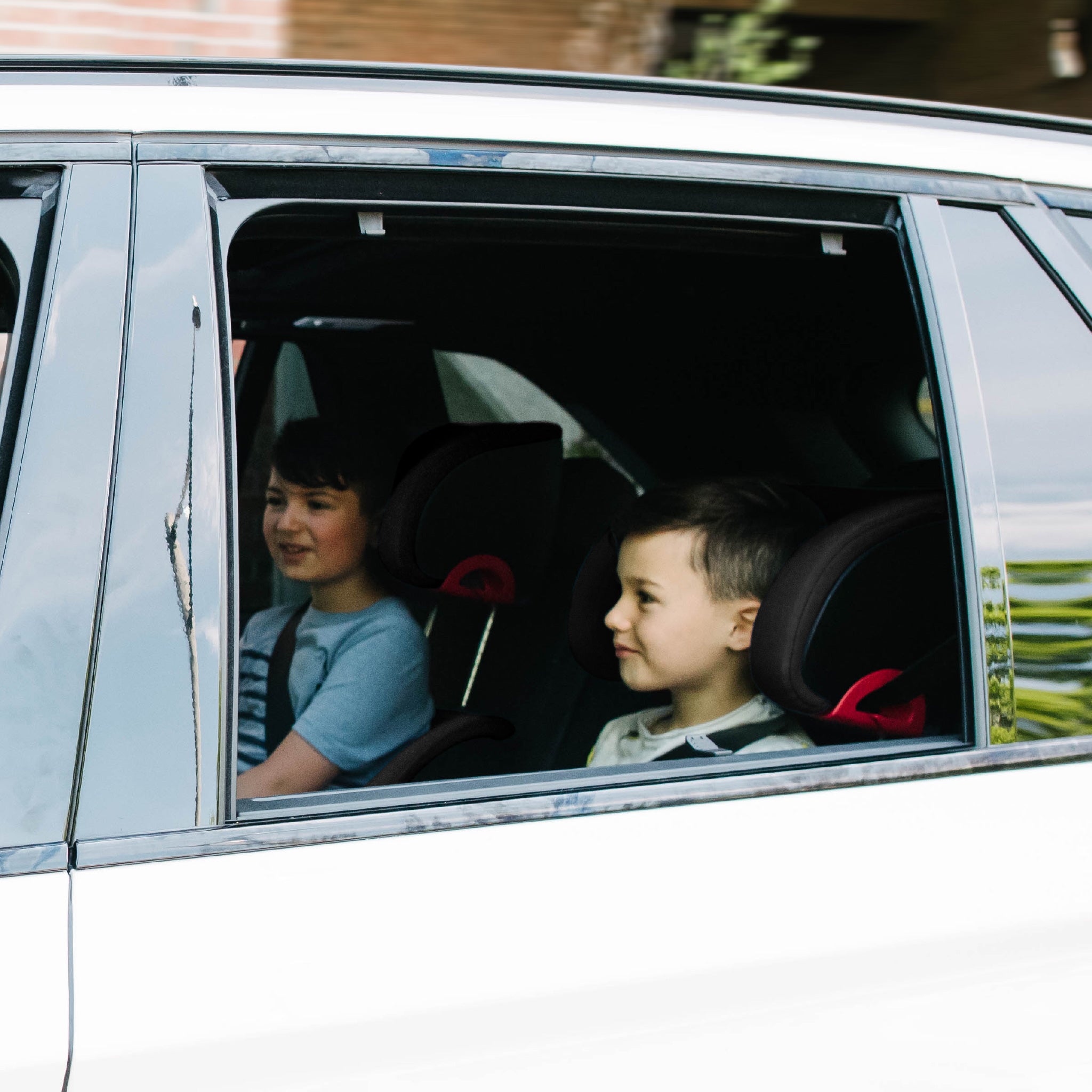 Two children sitting in a car riding in their Clek Oobrs all-groups