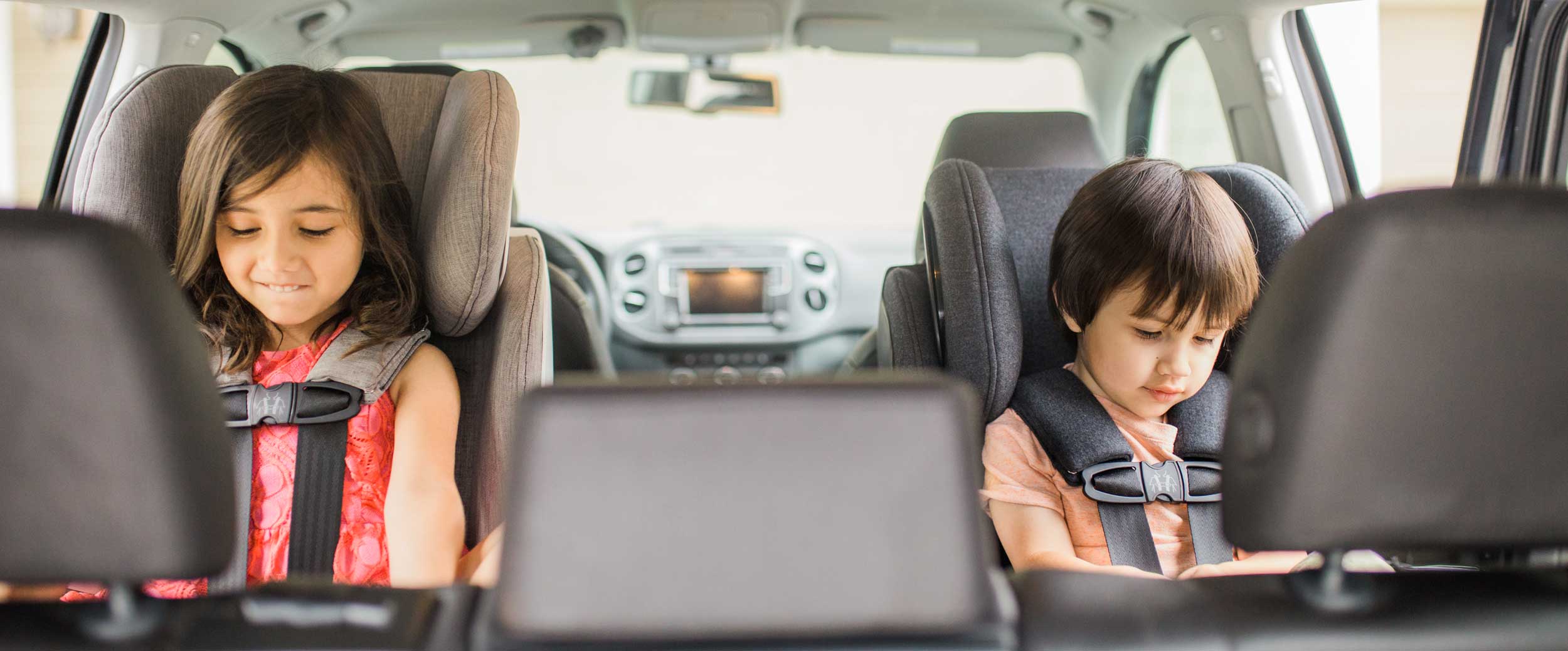 Brother and sister riding in their Clek convertible car seats in rear-facing mode