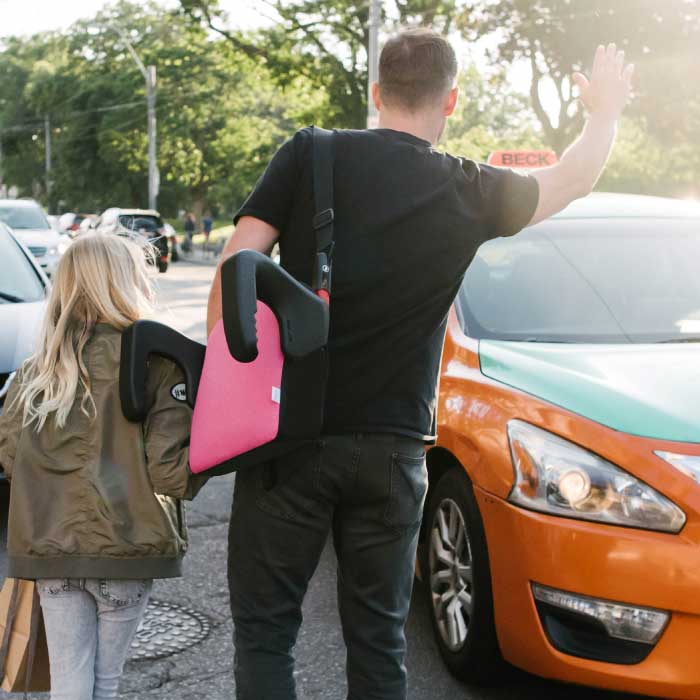 Father carrying his daughter's Clek Olli booster seat in Flamingo