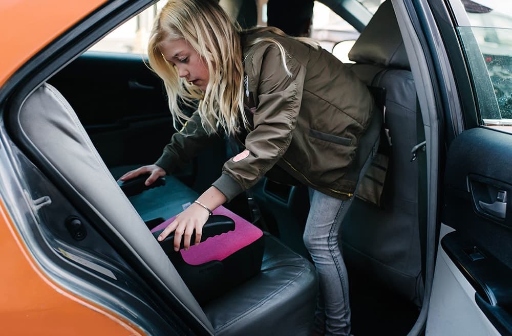 Young girl installing the Clek olli booster seat for kids in flamingo fabric