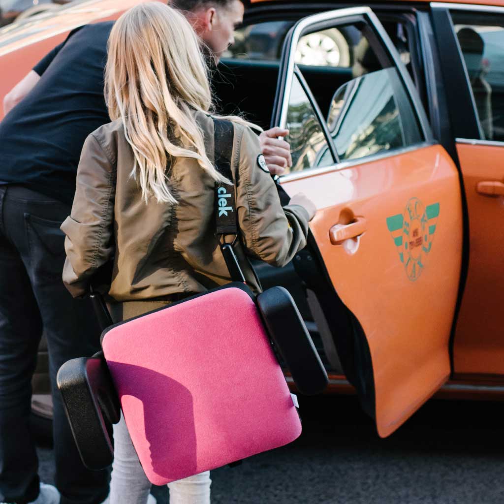Girl carrying her clek olli booster seat using strap-thingy accessory